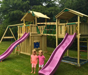 Houten speeltoestel met twee glijbanen, klimnet, netbrug en schommels in een tuin